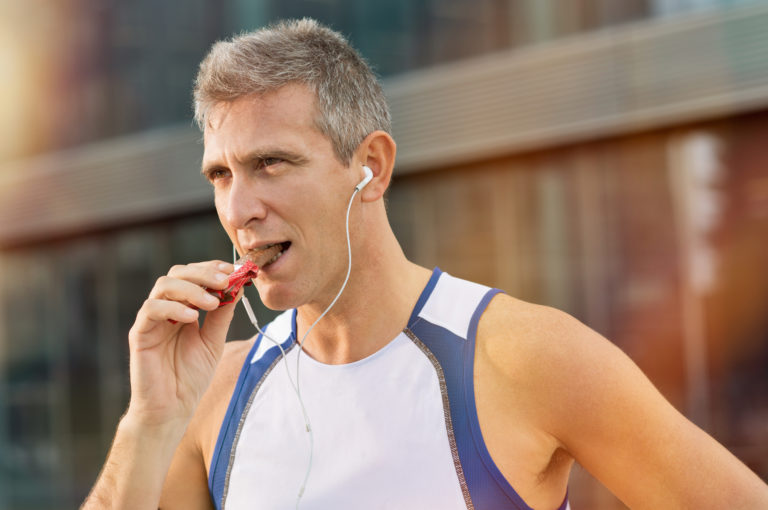 Older, fit man in a white shirt eating chocolate bar after a workout