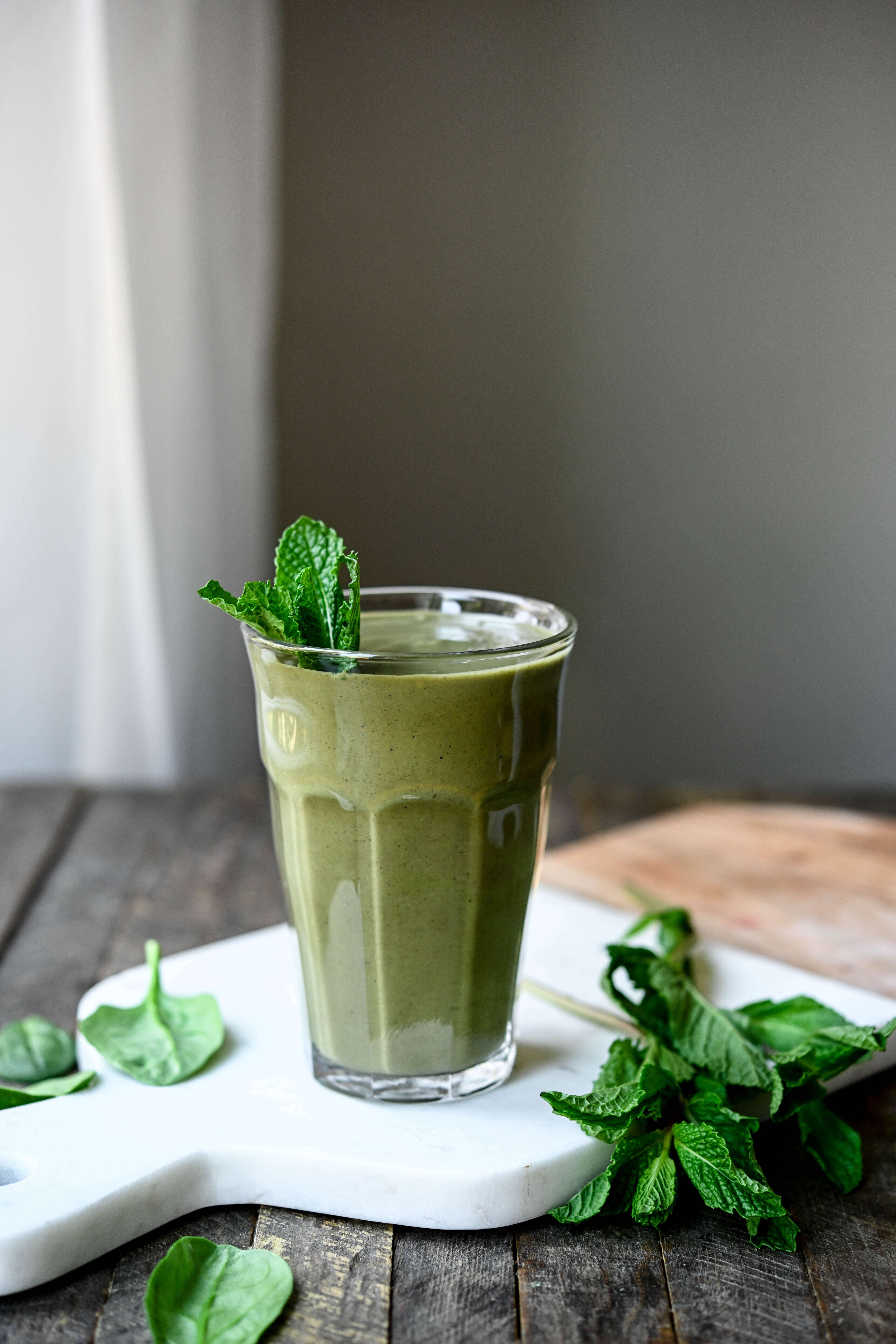 Side view of green chocolate smoothie garnished with mint on a marble serving tray