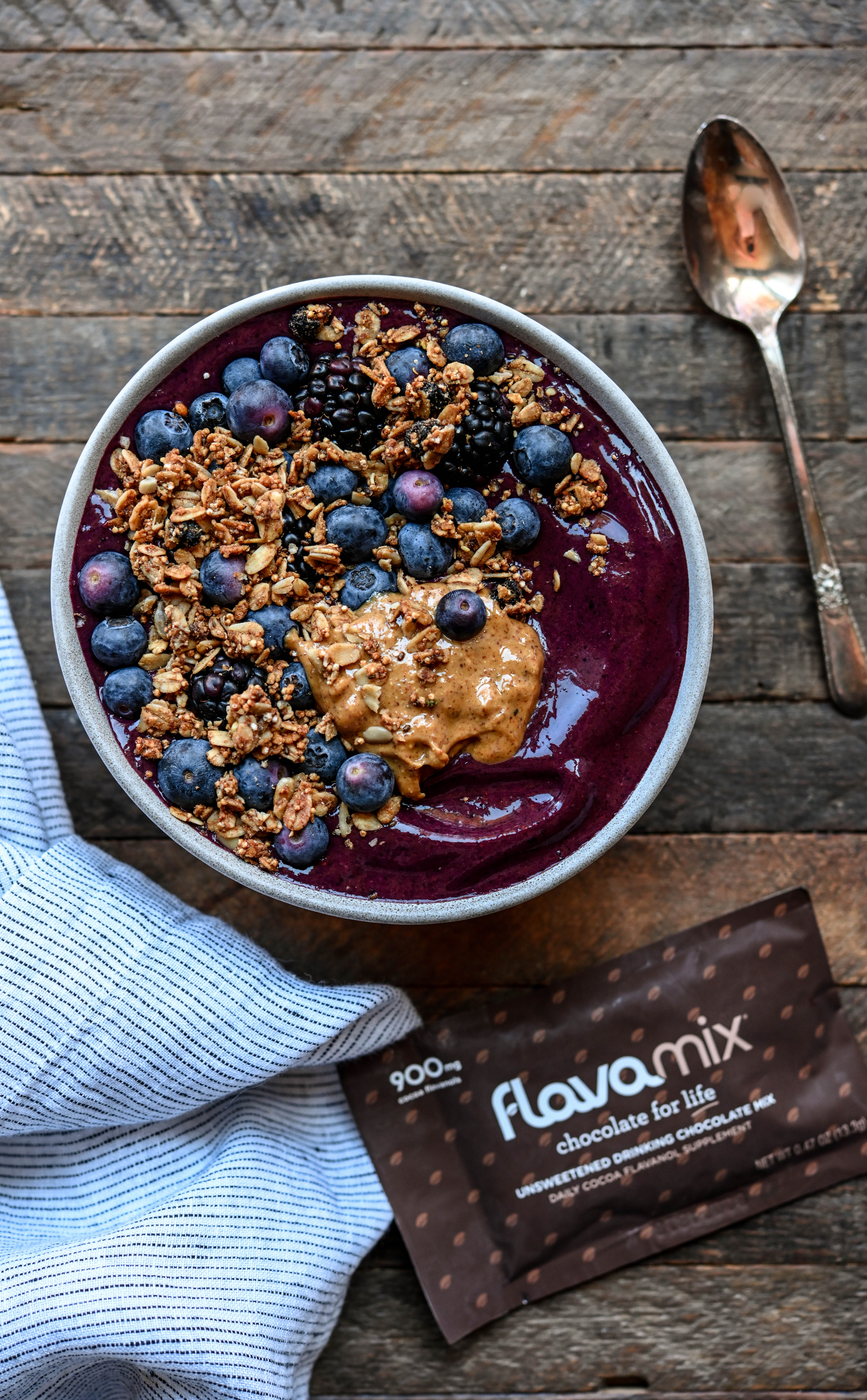 Overhead view of blueberry chocolate smoothie bowl with fresh blueberries, granola and almond butter on wood background